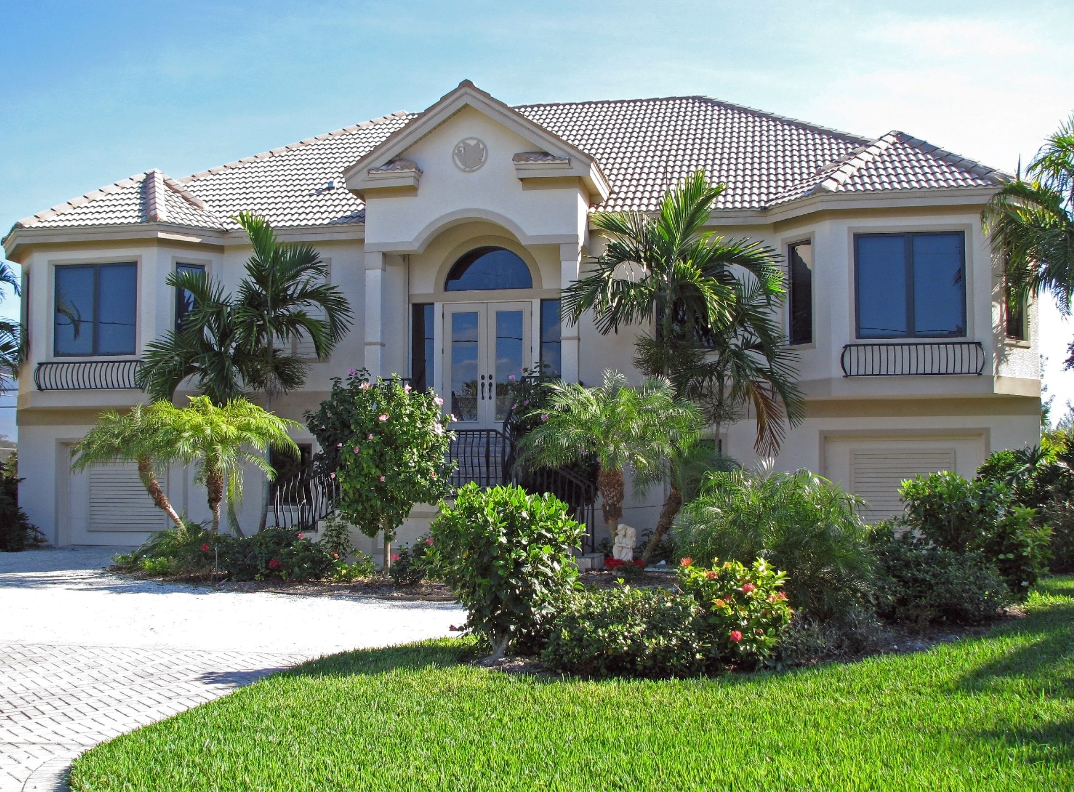 Luxury white two-story home with tile roof, palm trees, and manicured landscaping