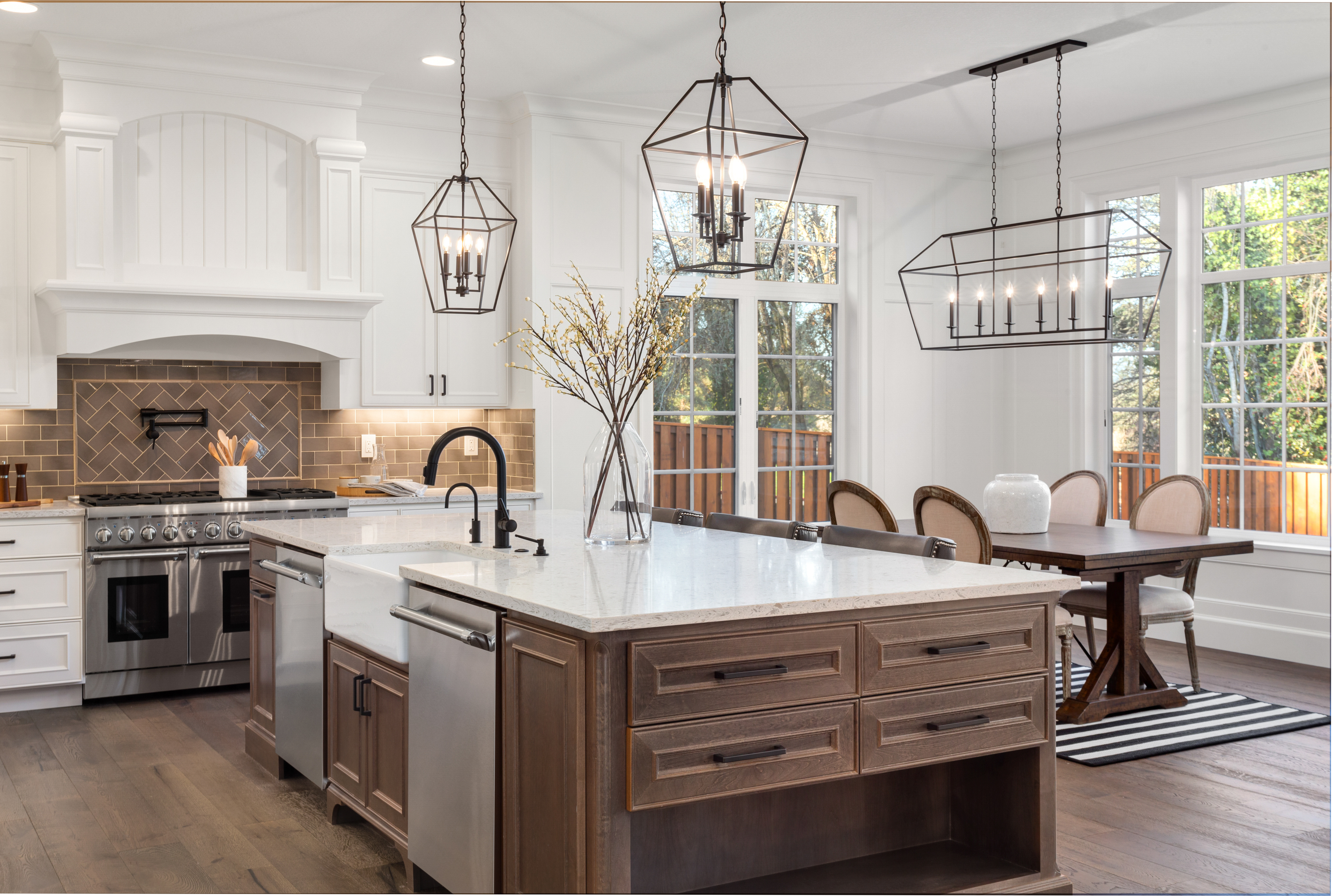 Modern kitchen with white cabinets, brown island, pendant lights, and dining area with forest views