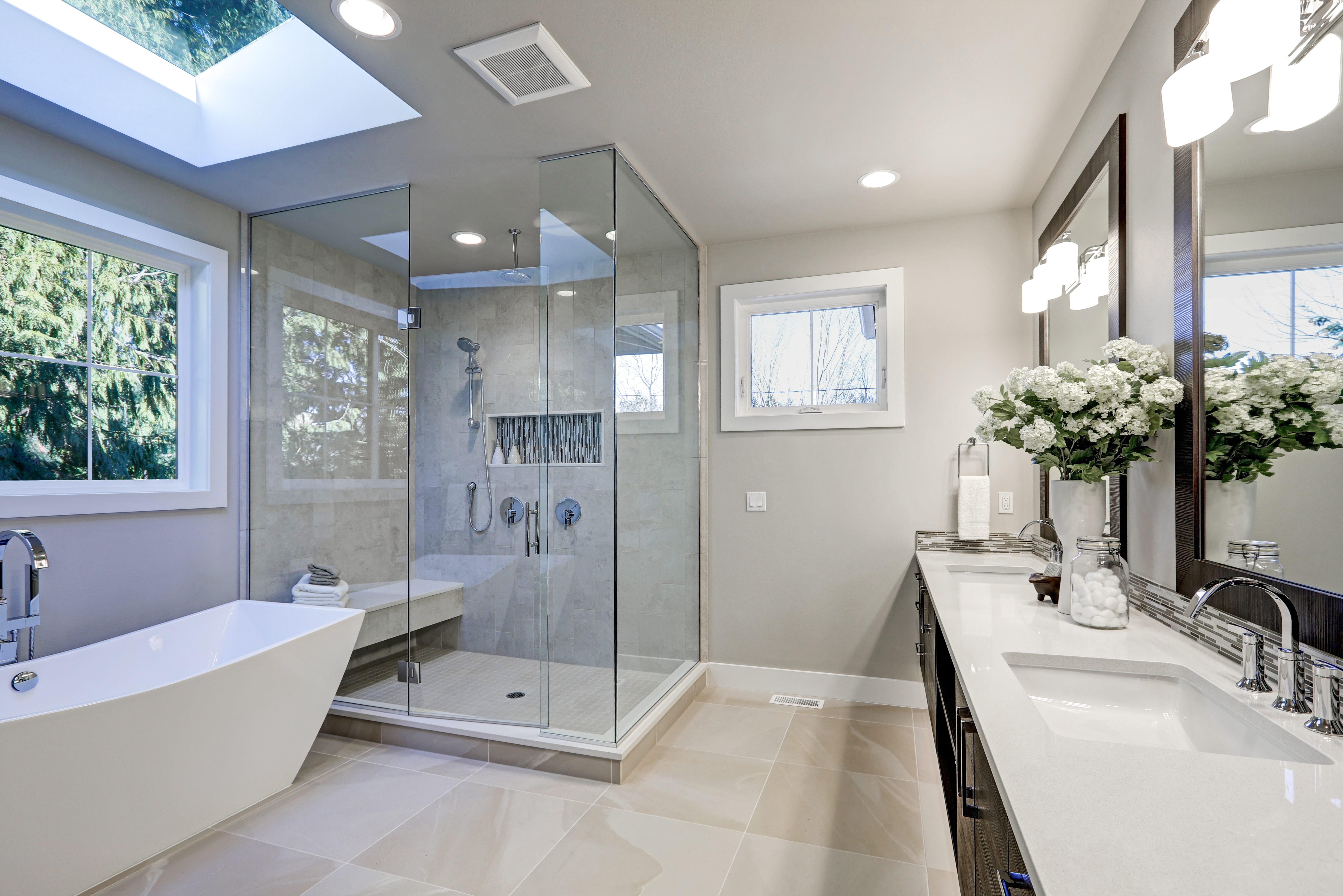 Modern luxury bathroom with glass-enclosed shower, freestanding tub, double vanity, and skylight