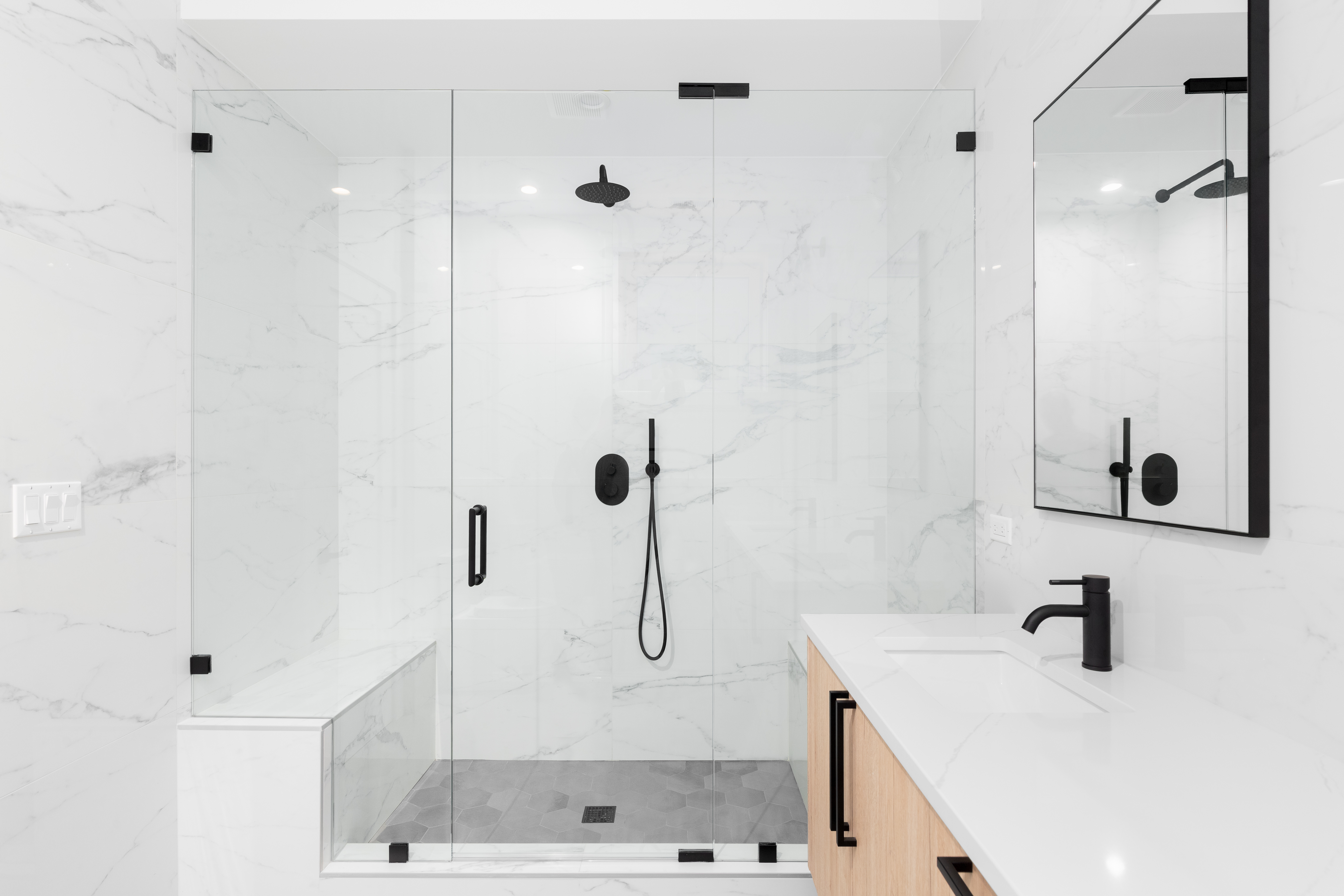 Modern white marble bathroom with glass shower enclosure and black fixtures