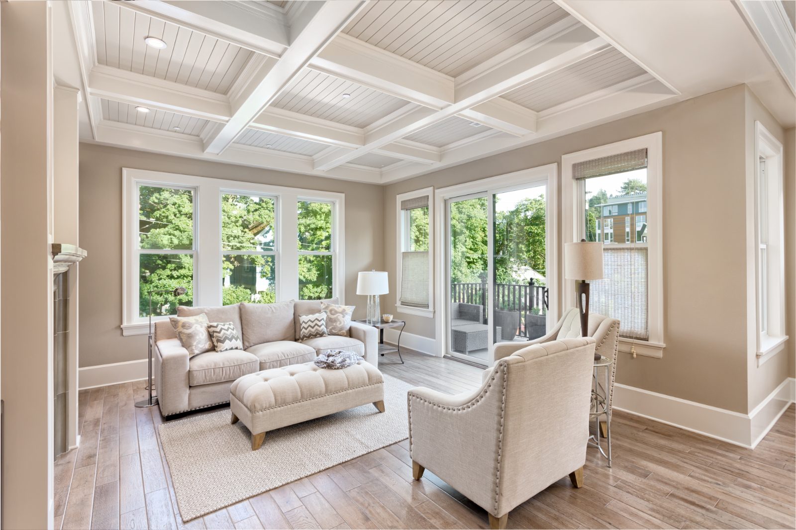 Bright sunroom with coffered ceiling, cream furniture, large windows overlooking trees and deck